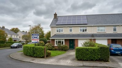 Irish suburban home with solar panels on slate roof and a for sale sign in front garden